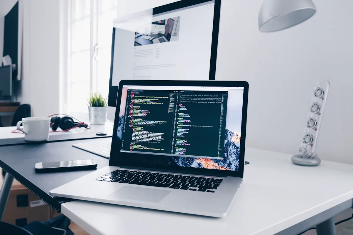 Modern workspace with a laptop displaying code, a coffee cup, and a notebook.